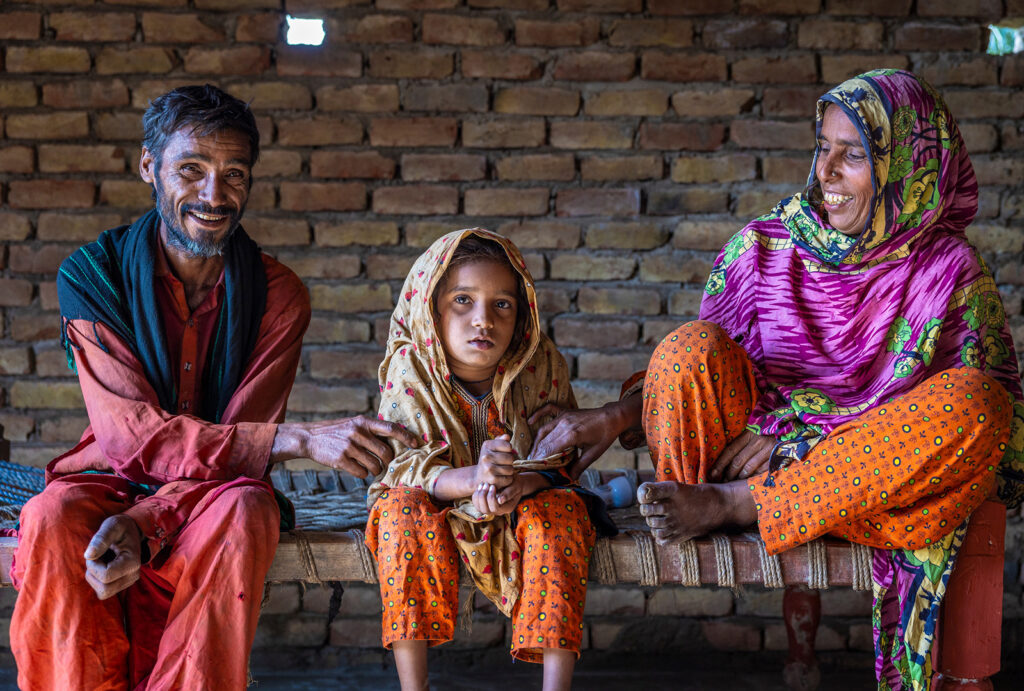 Ghulam, his wife, and their young daughter sit on a bench inside their new stone home.