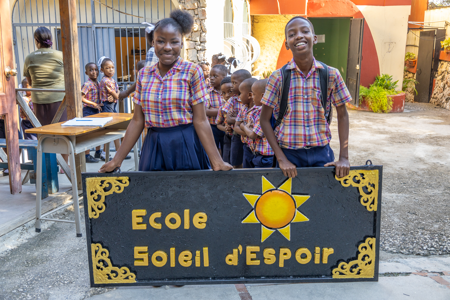 Students pose in front of a new metal sign for the School of Hope and Sunshine.