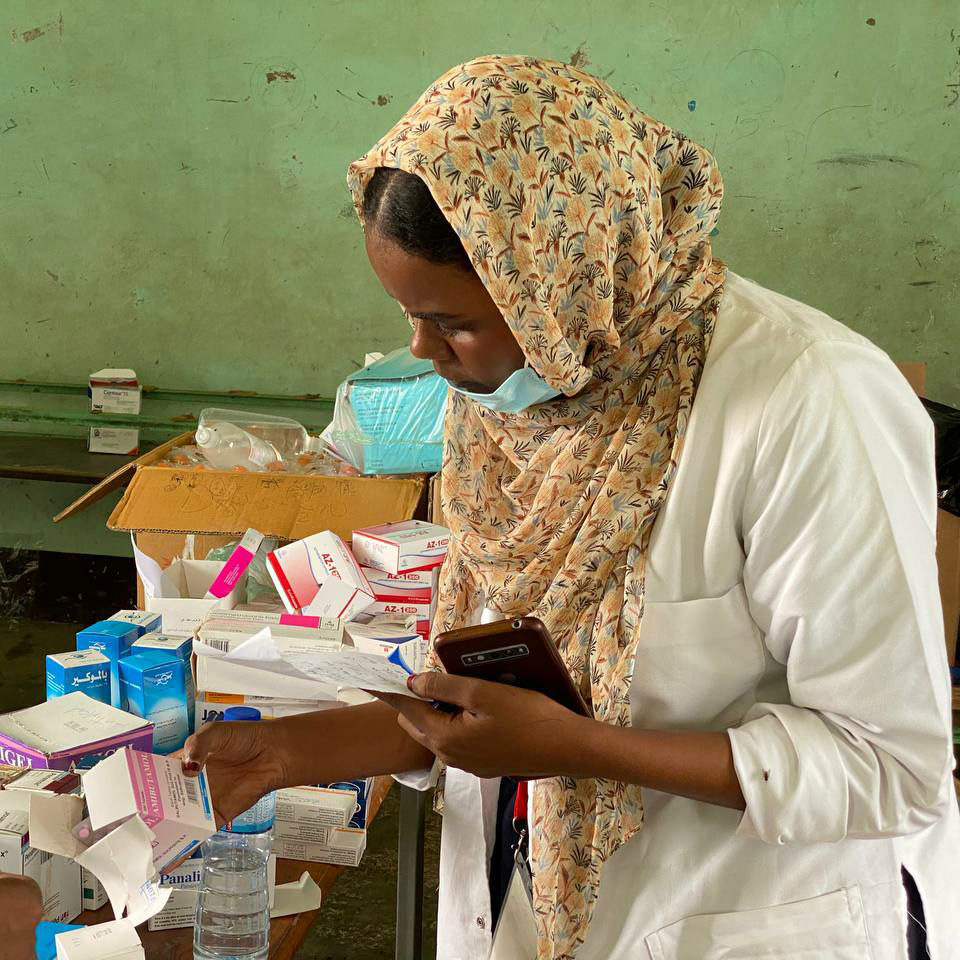 Sudanese nurse wearing a hijab assesses a table full of medical supplies.