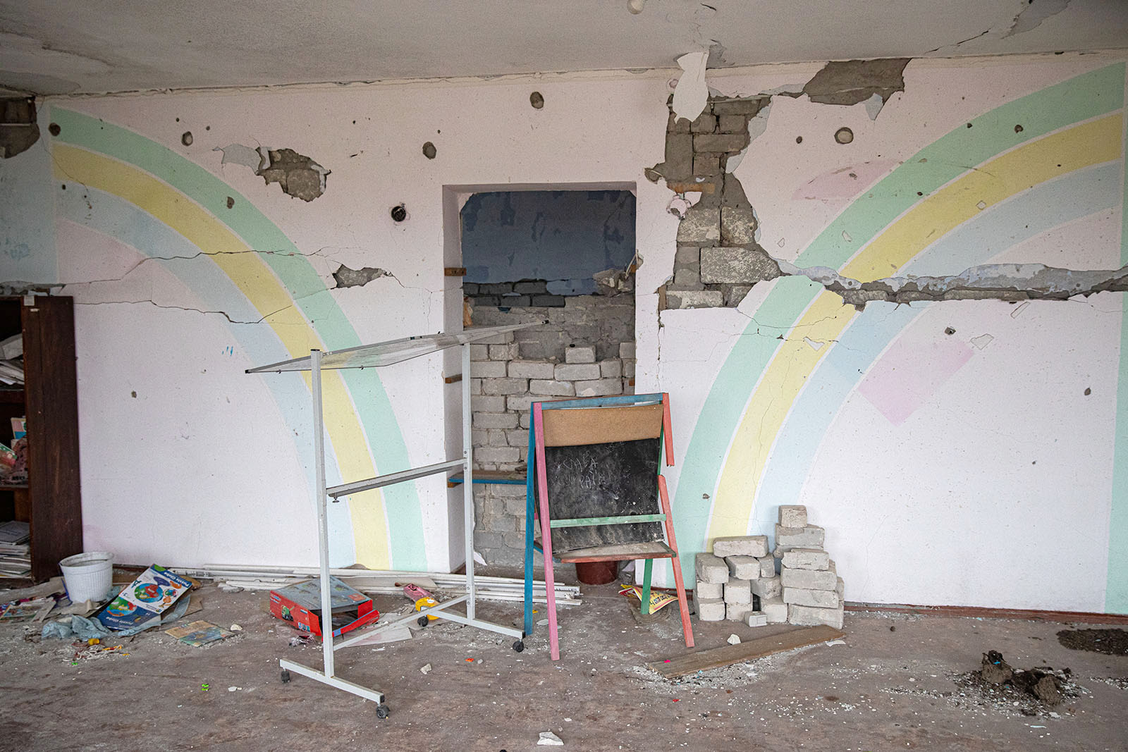 Classroom wall with painted rainbows has exposed brick and debris from the Russian attacks.