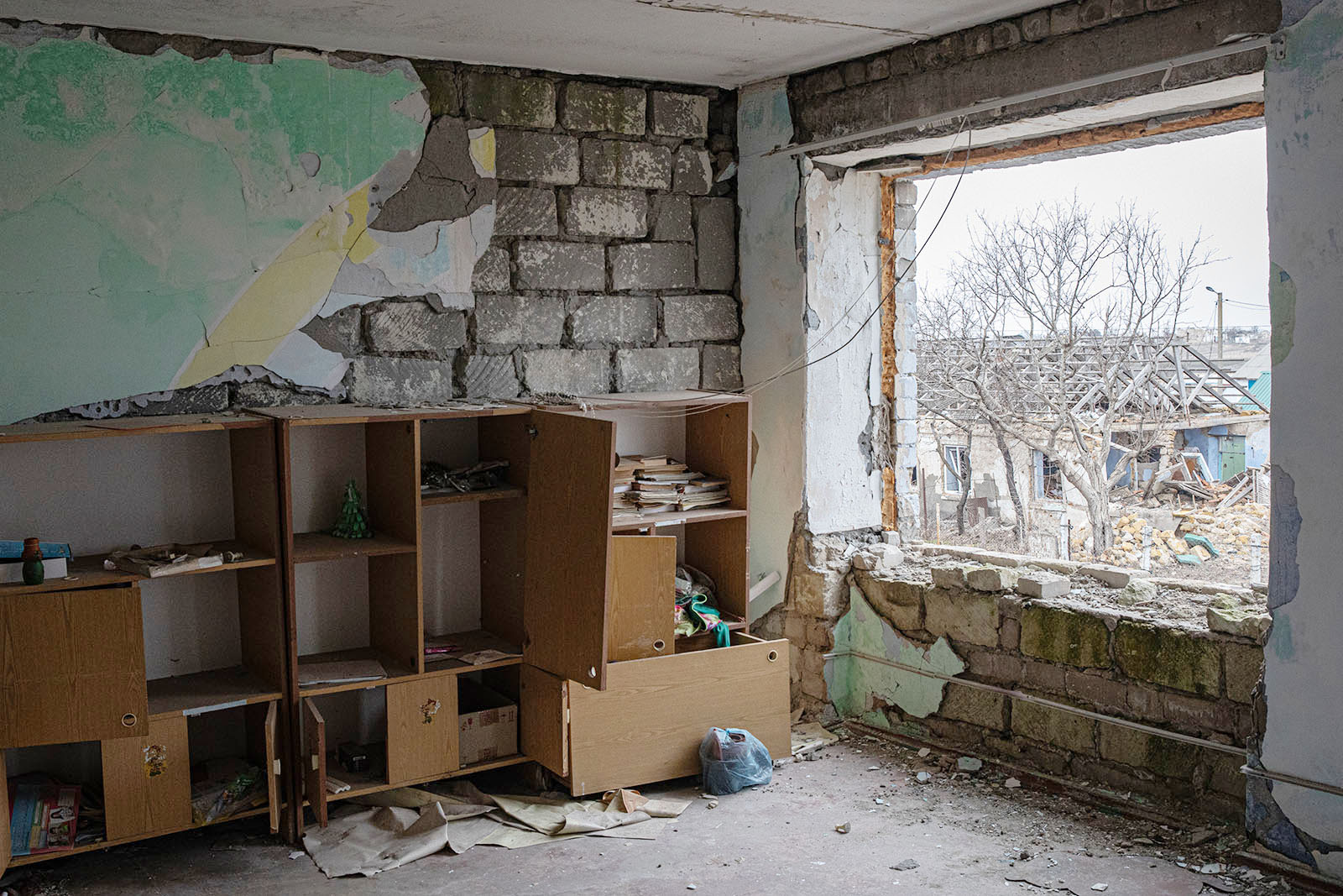 The inside of a damaged classroom reveals blown out window, debris on the floor, and damaged cubbies.