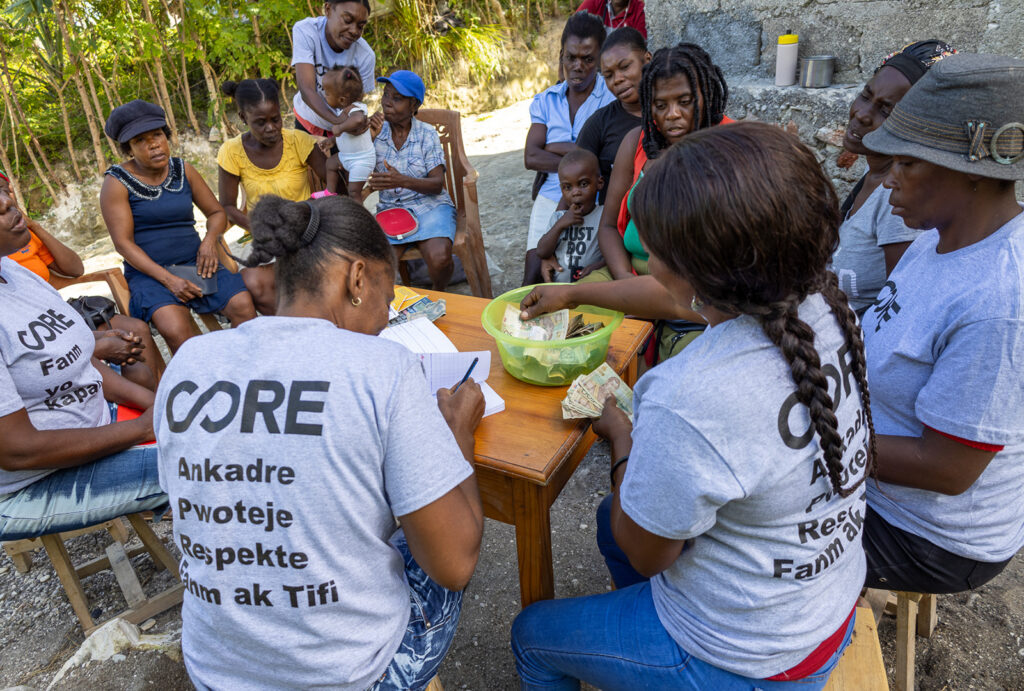 15 women sitting around a wooden table organizing paper money for financial skills training.