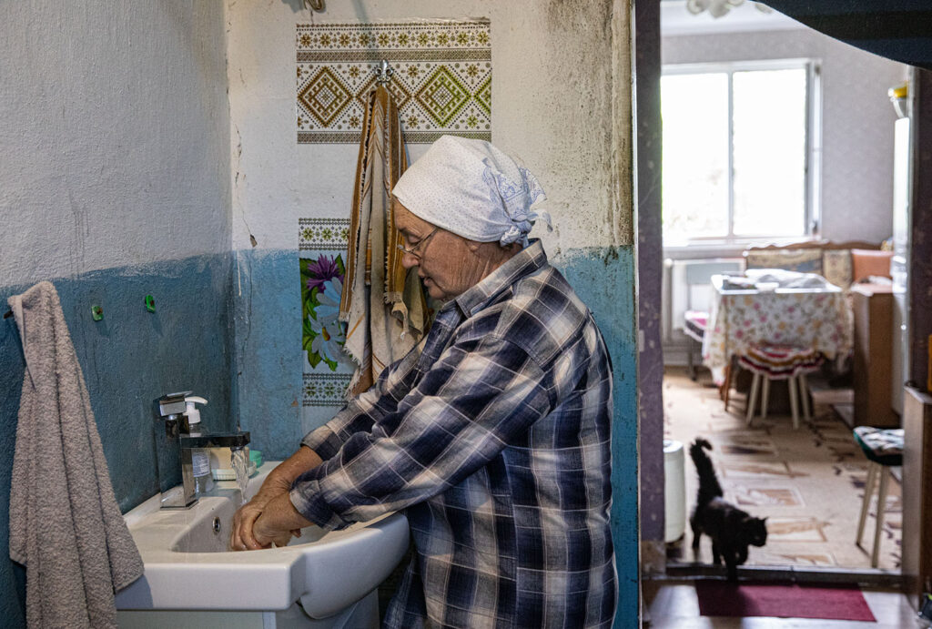 Elderly Ukrainian woman uses her sink inside her home.