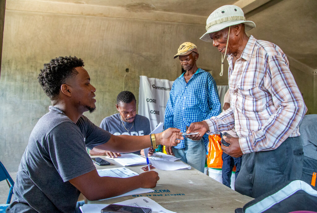 A member of CORE's staff sits and a table and receives information from a man looking to receive a food kit.