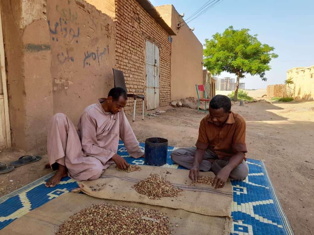 Two men sort and weigh beans to distribute at a community kitchen in Sudan.