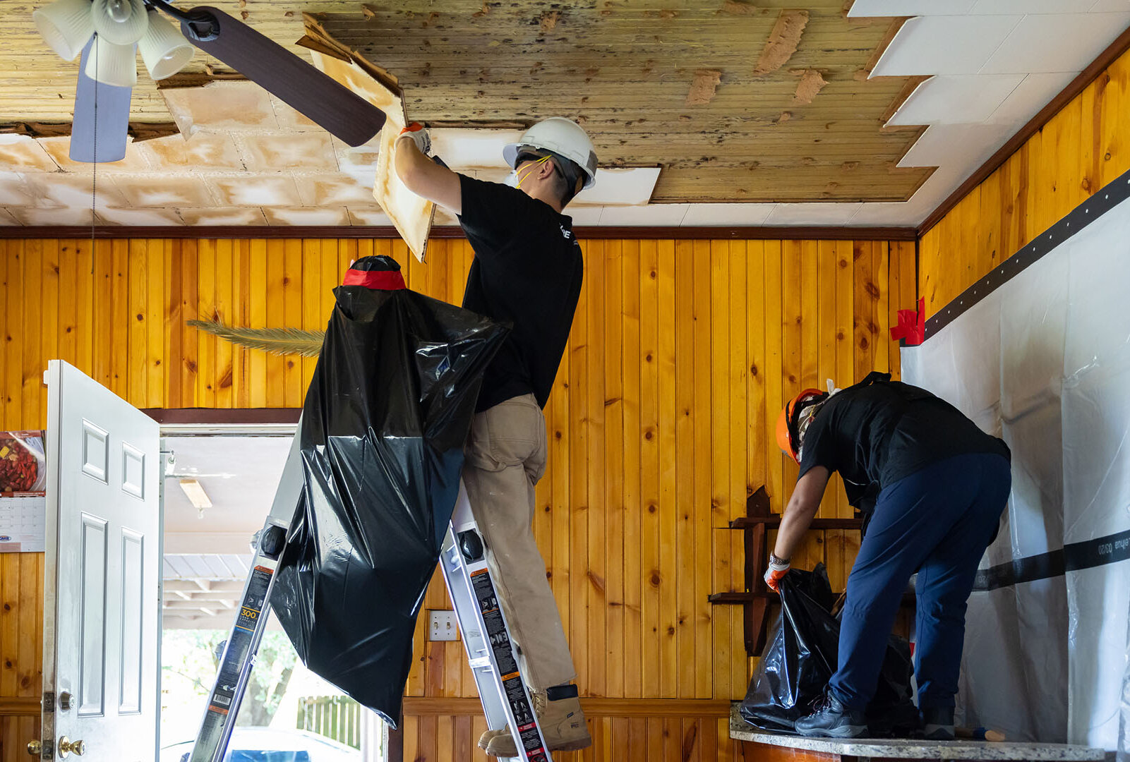 CORE staff inside a water-damaged home removing panels from ceiling