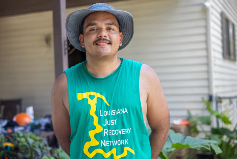 Axel wearing a hat and sleeveless LJRN shirt posing in front of a mobile home he helped repair.