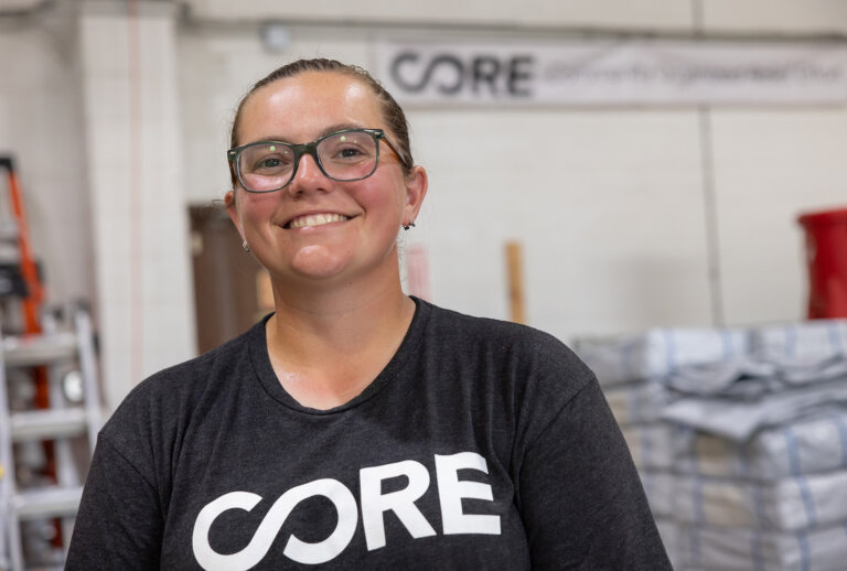 Kirsty wears glasses and is posing in CORE's Louisiana warehouse