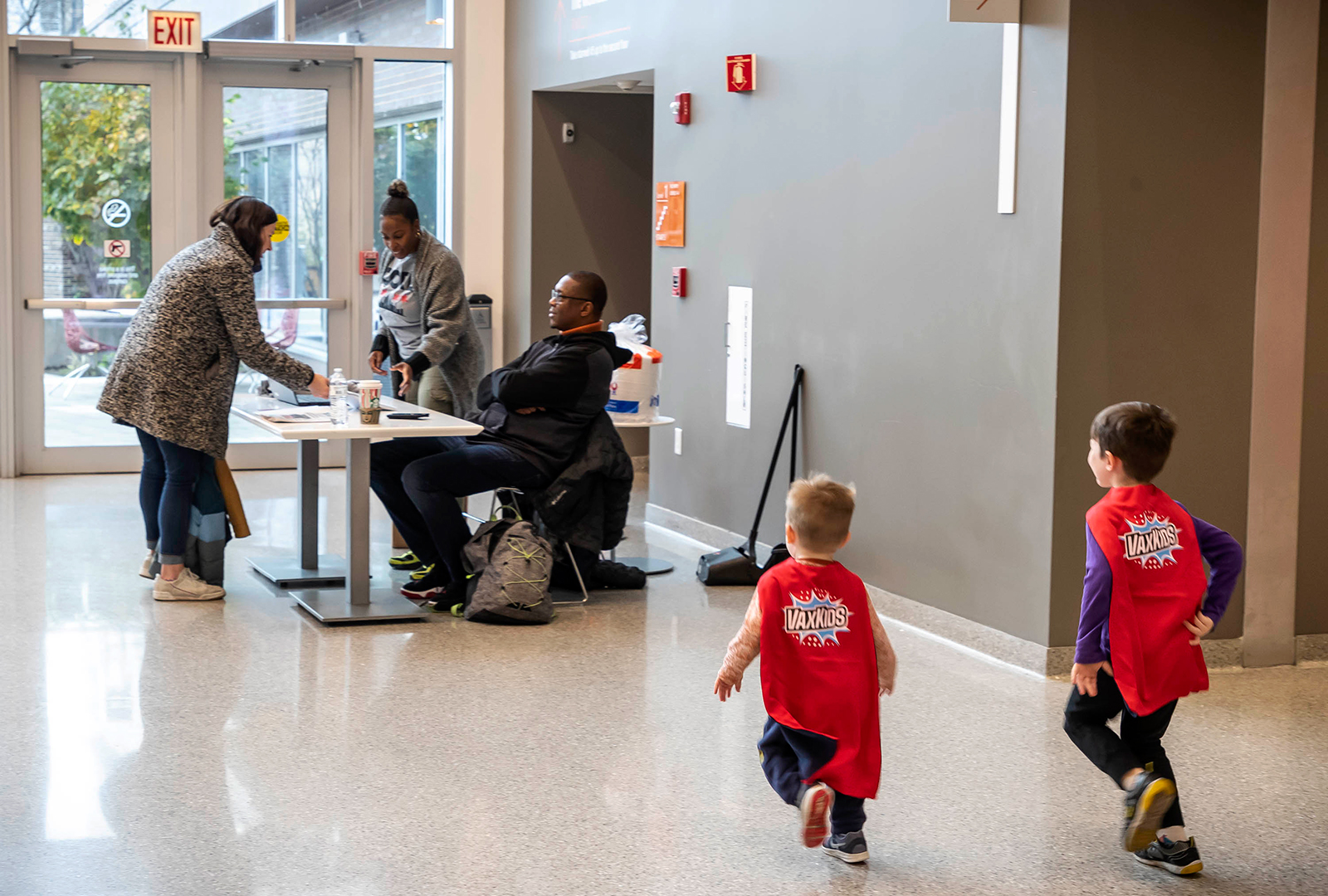 Two young boys run with capes toward a registration table.