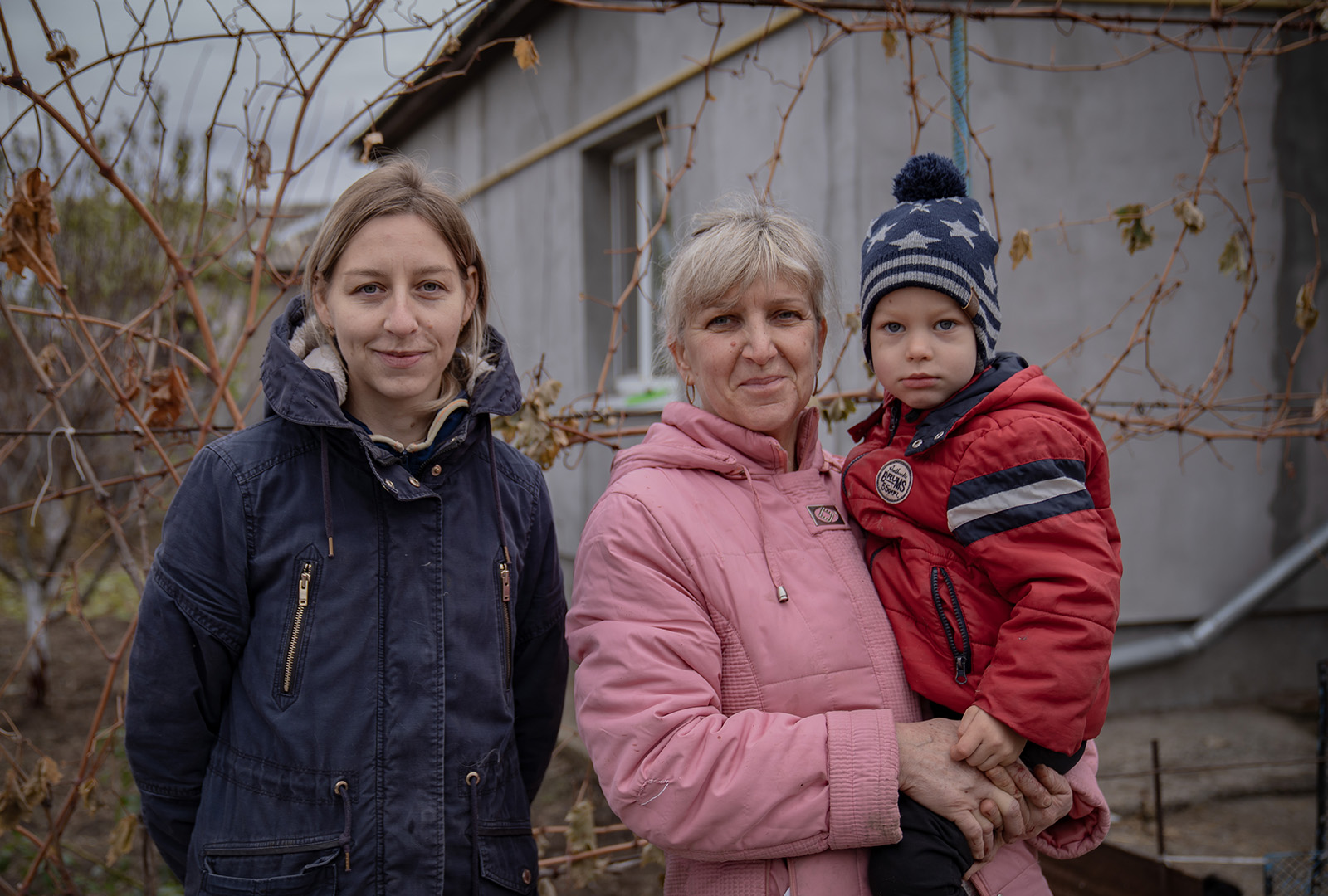 A family, a grandmother, mother and child stand outside of their home in Ukraine.