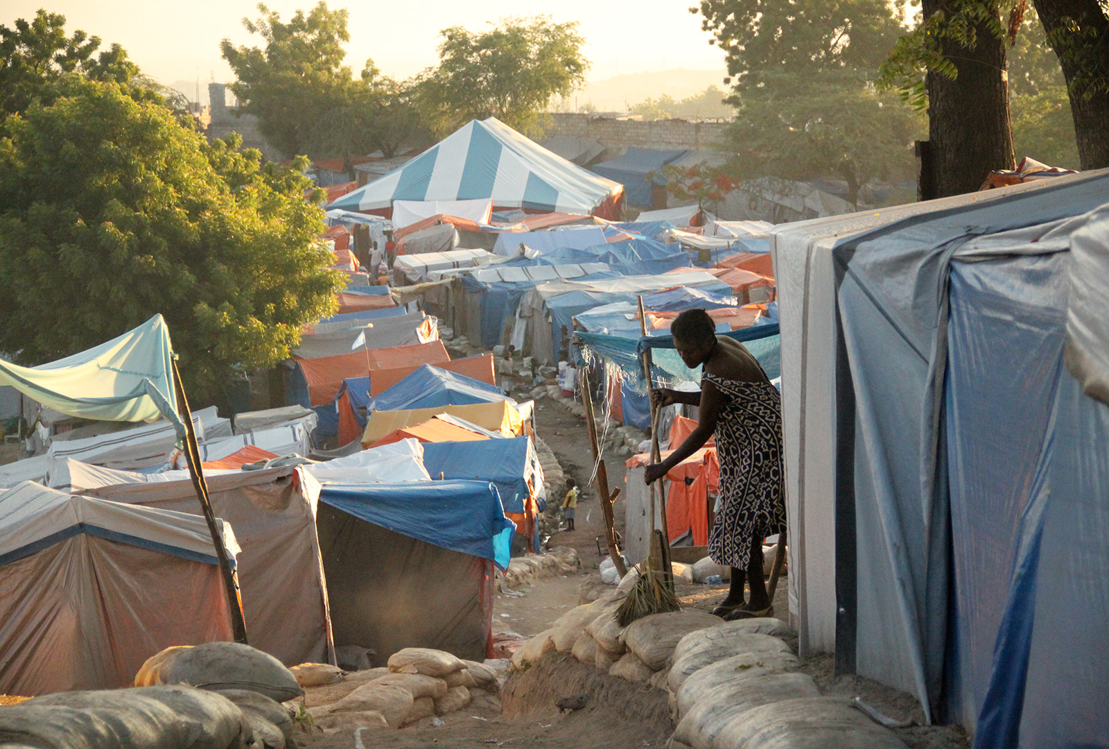 A woman sweeps the path in front of her tent shelter in the Petionville Club Camp in early 2010. At its height, more than 60,000 displaced Haitians called the Petionville Club camp home. There, J/P HRO offered medical and dental services, set-up a school and community center, and assisted with relocations as part of camp management.