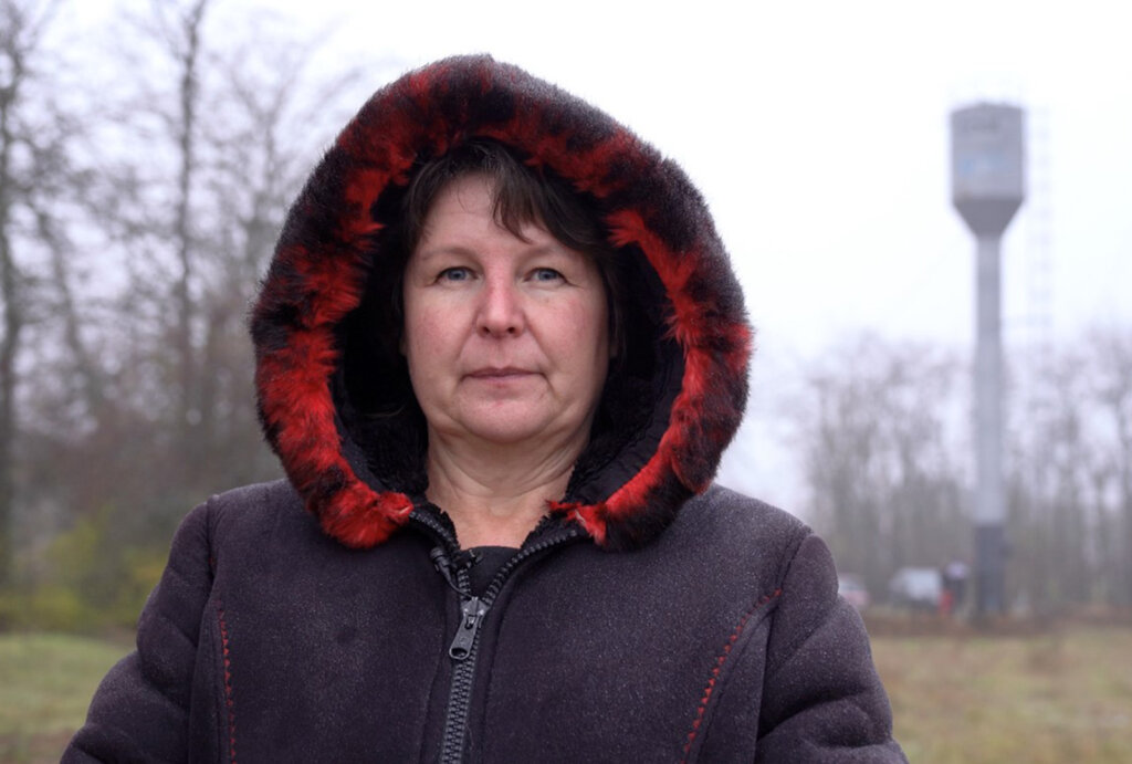 A woman in Ukraine poses for a photo with a repaired water tower in the background.